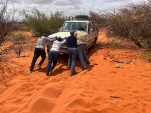 People push a jeep stuck in sand